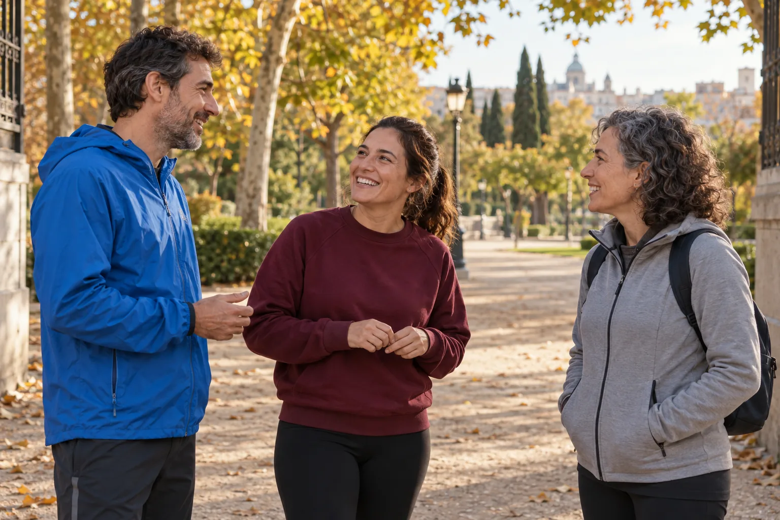 Tres personas conversan al comienzo de un paseo en un parque de otoño.