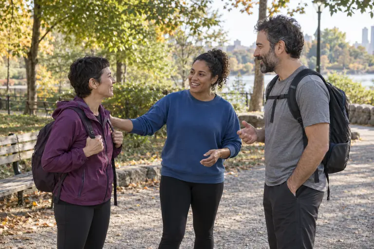 Tres personas adultas conversan al encontrarse en un parque.